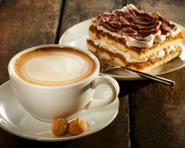 Cup of double espresso coffee with piece of cake on wooden table